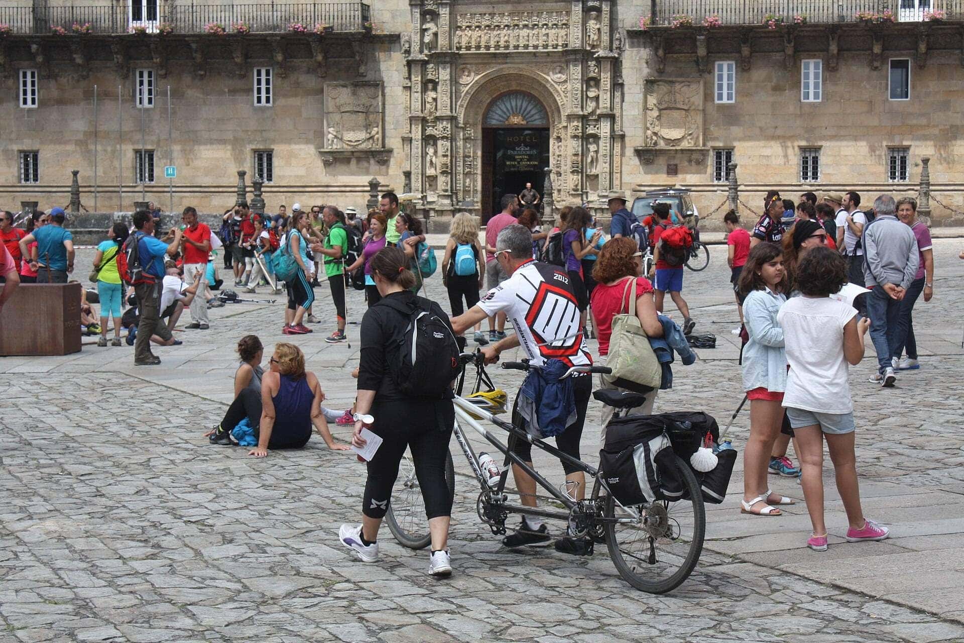 Peregrinos con mochilas y una bicicleta de tándem en la Praza do Obradoiro, frente al Hostal dos Reis Católicos